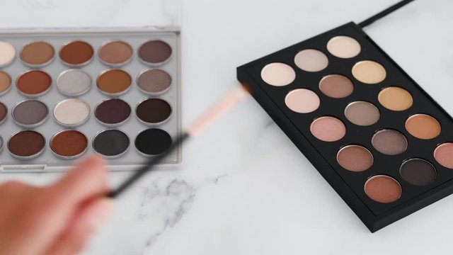 eyeshadow palettes with nudes and bronzy tones and hand placing brushes next to them on marble tabletop