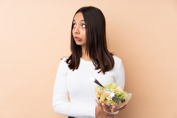 Young brunette girl holding a salad over isolated background with confuse face expression