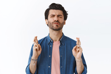 Man eager receive promotion, cross fingers good luck, bite lip and close eyes as praying, want...