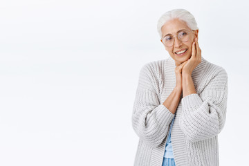 Tenderness, family and aging concept. Old smiling, happy senior woman in glasses with grey hair, looking delighted and cheerful camera, grinning as touching face and contemplate grandchild playing