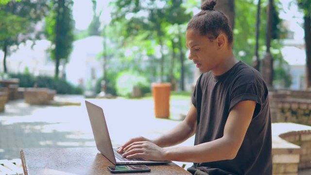 side view overworked trendy guy working sitting in park student typing on computer summer outdoor background