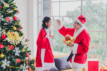 Obraz premium Asian father and daughter wear Santa Claus outfits. He gave her gifts on the occasion of Christmas and New Year. In the living room decorated the room to celebrate the important day of the family.