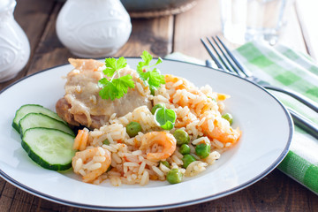 Paella with chicken, shrimp and vegetables on a white plate on a wooden table, selective focus