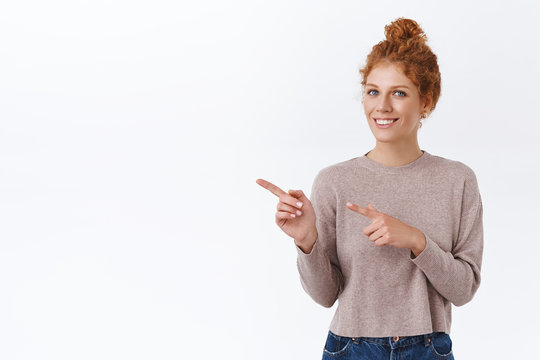 Tender, Elegant Redhead Woman With Curly Hair In Bun, Wear Cozy Sweater, Pointing Fingers Left, Asking Question About Product, Smiling At Camera, Advertise Something Over White Background