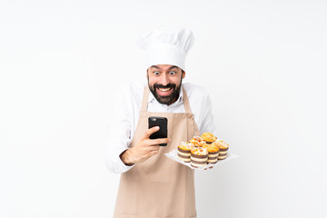 Young man holding muffin cake over isolated white background surprised and sending a message