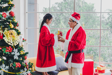 Asian father and daughter wear Santa Claus outfits. He gave her gifts on the occasion of Christmas and New Year. In the living room decorated the room to celebrate the important day of the family.