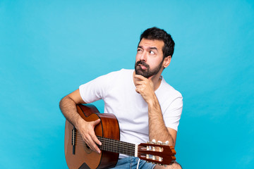Young man with guitar over isolated blue background with confuse face expression