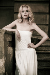 Naklejka premium Black-and-white photo of a beautiful young woman in a white dress descends the stairs on the background of an old building with doors. Gothic romance concept