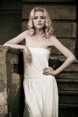 Black-and-white photo of a beautiful young woman in a white dress descends the stairs on the background of an old building with doors. Gothic romance concept