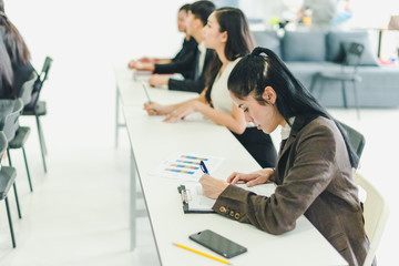 Asians attend seminars and listen to lectures from speakers in the training room. Some people take notes. Some people raised their hands to ask the narrator. 