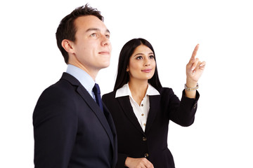 A young business woman is pointing while a young business man is looking up. They are smiling.