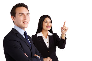 A young business woman is pointing while a young business man is looking up. They are smiling.