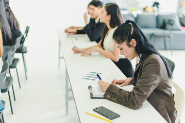 Asians attend seminars and listen to lectures from speakers in the training room. Some people take notes. Some people raised their hands to ask the narrator. 