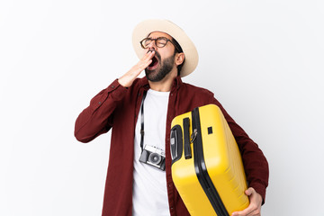 Traveler man man with beard holding a suitcase over isolated white background yawning and covering wide open mouth with hand