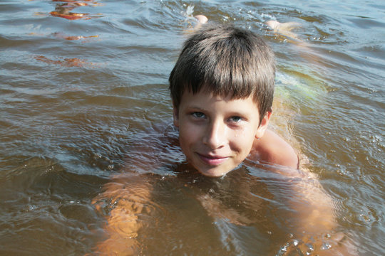 Boy - brunette in the water in shallow water in the river. Russian