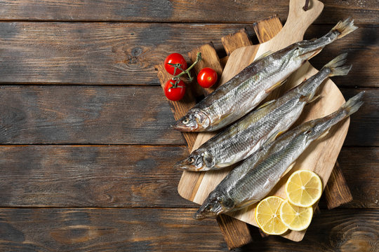 Smoked or dried smelt fish on a wooden Board on a brown wooden table. Top view with space for text	