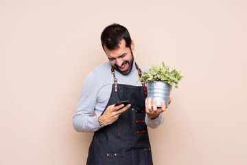 Man holding a plant over isolated background with phone in victory position