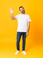 Full-length shot of man with beard over isolated yellow background saluting with hand with happy expression © luismolinero