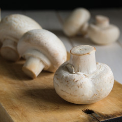 still life, champignon mushrooms on a cutting wooden board with black background