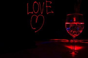 Red Laser light painting of Love sign for valentines day in a dark background with wine glass for...