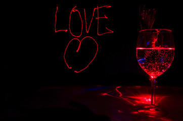 Red Laser light painting of Love sign for valentines day in a dark background with sparkling  wine...