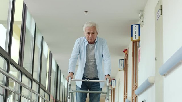 asian old man walking using a walker in hallway of nursing home