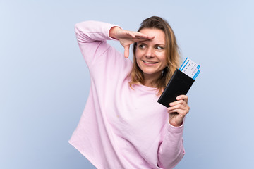 Fototapeta premium Blonde woman over isolated background in vacation with passport and plane tickets while looking something in the distance