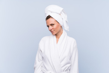 Woman in bathrobe over isolated blue background standing and looking to the side