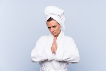 Woman in bathrobe over isolated blue background pleading