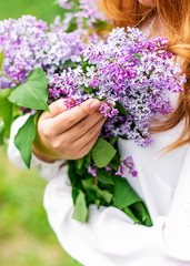 Spring background. Flowers of lilac in the hands of a young girl in a white blouse. Close up, copy space
