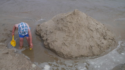 Dziecko na plaży bawi się w piasku nad morzem. Chłopiec z wiaderkiem i łopatką buduje zamki z...