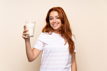 Teenager redhead girl holding a glass of milk over isolated background smiling a lot