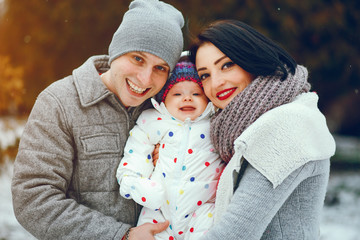 Fototapeta premium A young cheerful family in winter clothes walks in a snowy park