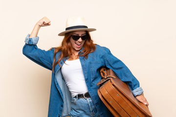 Redhead traveler girl with suitcase over isolated background celebrating a victory