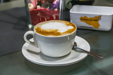 A white cup with hot cappuccino coffee with steam foam saucer and teaspoon