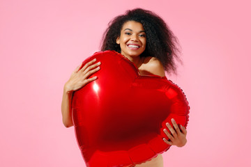 Happy girl holds red heart shape balloon. Photo of smiling young girl in love on pink background. Valentine's Day