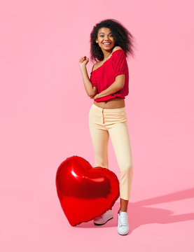 Happy girl witg red heart shape balloon. Photo of smiling young girl in love on pink background. Valentine's Day