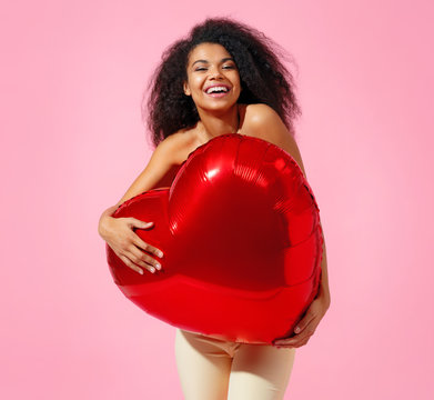 Happy girl holds red heart shape balloon. Photo of smiling young girl in love on pink background. Valentine's Day