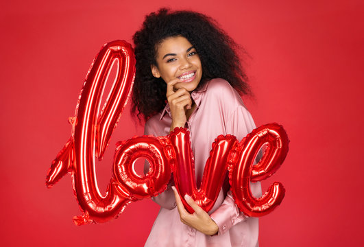 Cute girl holds letter shaped balloon. Photo of smiling young girl in love on red background. Valentine's Day