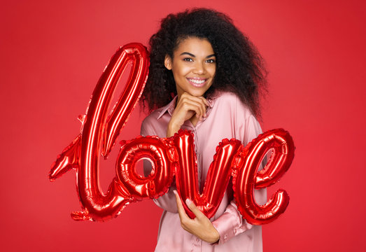 Cute girl holds letter shaped balloon. Photo of smiling young girl in love on red background. Valentine's Day