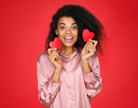 Happy girl holds red papers hearts and smiling. Photo of attractive latin girl in love on red background. Valentine's Day