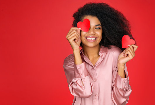 Happy girl holds red papers hearts and smiling. Photo of attractive latin girl in love on red background. Valentine's Day