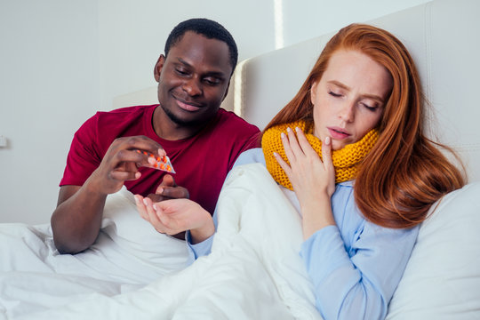african american man in knitted scarf and redhaired ginger woman in pajamas lying in bed day off from work because they are feel bad mood - Powered by Adobe