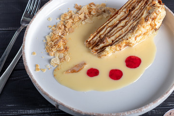 Napoleon dessert with custard, condensed milk sauce, crumbs of dough and raspberry jam. In the background is a cappuccino. On a wooden natural background.