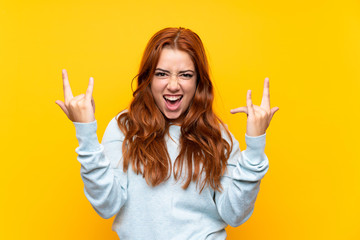 Teenager redhead girl over isolated yellow background making rock gesture