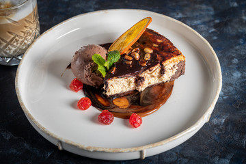 Chocolate dessert with a scoop of coffee ice cream, slices of dried cherry and a slice of orange. Garnished with mint leaves. Cappuccino in the background.