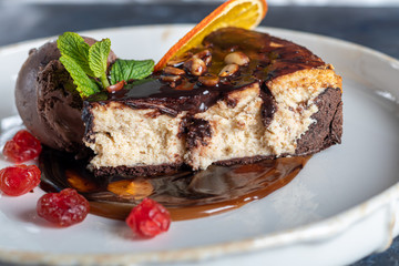Chocolate dessert with a scoop of coffee ice cream, slices of dried cherry and a slice of orange. Garnished with mint leaves. Cappuccino in the background.