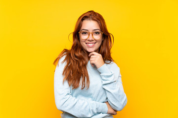 Teenager redhead girl over isolated yellow background with glasses and smiling
