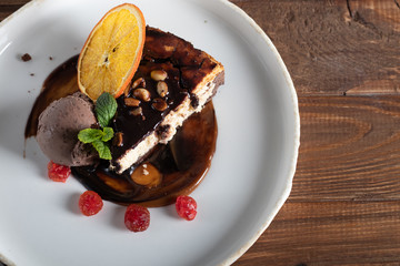 Chocolate dessert with a scoop of coffee ice cream, slices of dried cherry and a slice of orange. Garnished with mint leaves. Cappuccino in the background. On a dark background.