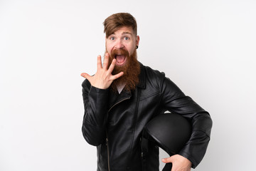 Redhead man with long beard holding a motorcycle helmet over isolated white background with surprise facial expression